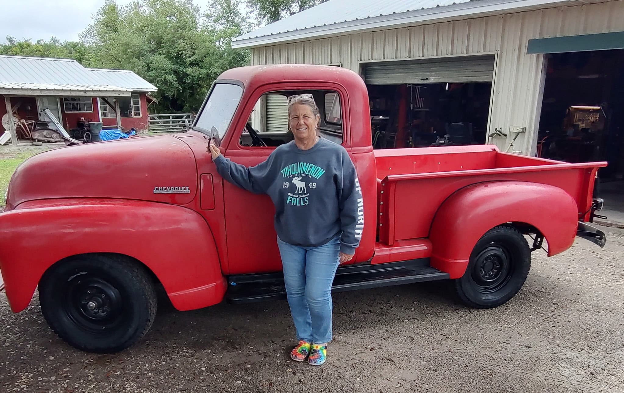 Sandi beside a restored red 1949 Chevrolet pickup outside the farm workshop